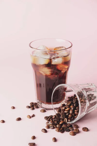 Glasses with cold brew and coffee beans on pink background