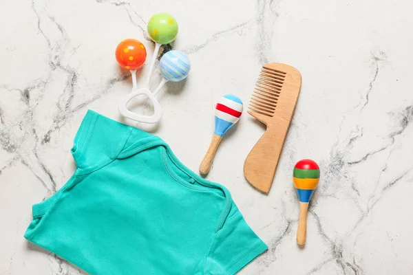 Bebek kıyafeti, tahta saç tarağı ve beyaz mermer arka planda çıngırak.