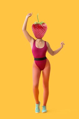 Kafası yerine olgun çilekli kadın sarı arka planda aerobik yapıyor.