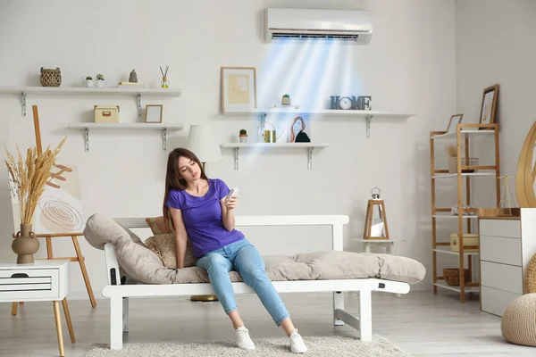 Young woman switching on air conditioner in room