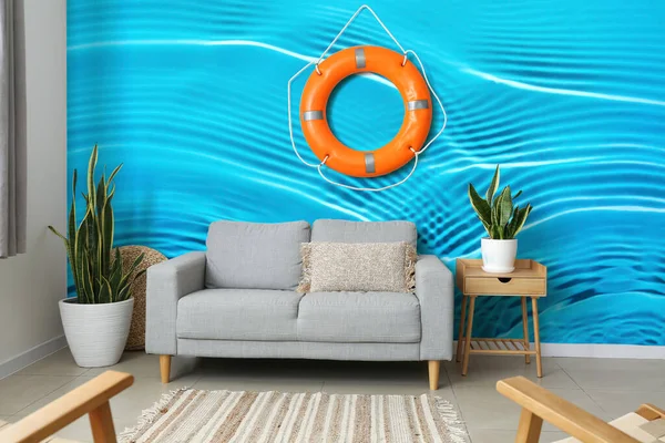 Interior of modern living room with sofa near wall with lifebuoy and print of clear blue water