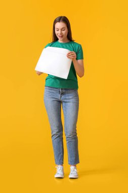 Sarı arka planda zarfı olan güzel genç bir kadın.