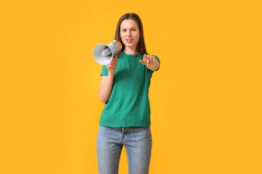 Güzel genç bir kadın megafona bağırıyor ve sarı arka plandaki izleyiciye işaret ediyor.