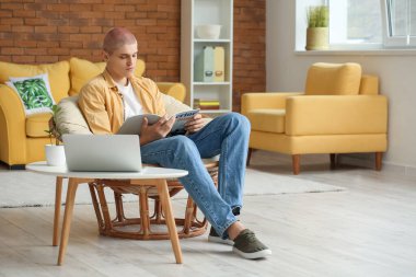 Evdeki koltukta dergi okuyan genç adam.