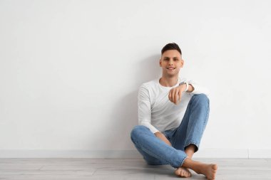 Akıllı, çıplak ayaklı genç adam ışık duvarının yanında oturuyor.