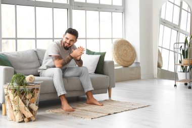 Evdeki kanepede oturan yakışıklı çıplak ayaklı adam.