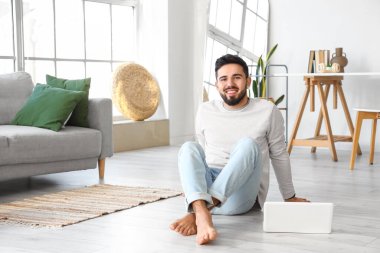 Evde dizüstü bilgisayarı olan yakışıklı, çıplak ayaklı bir adam.