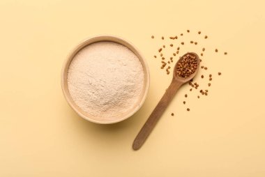 Bej arka planda karabuğday taneli bir kase un ve kaşık.