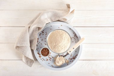 Üzerinde un kaseleri, karabuğday taneleri ve beyaz ahşap arka planda kaşık olan tepsi.