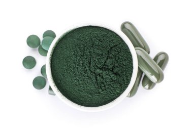 Bir kase spirulina tozu ve beyaz arka planda haplar.