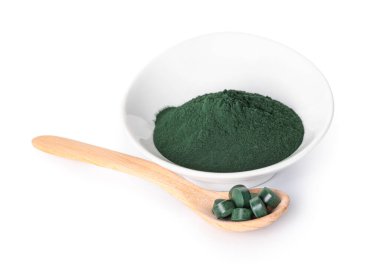 Beyaz arka planda haplı bir kase spirulina tozu ve kaşık.