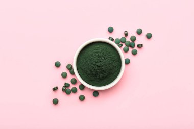 Bir kase spirulina tozu ve pembe arka planda haplar.