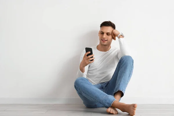 Young barefoot man using mobile phone near light wall