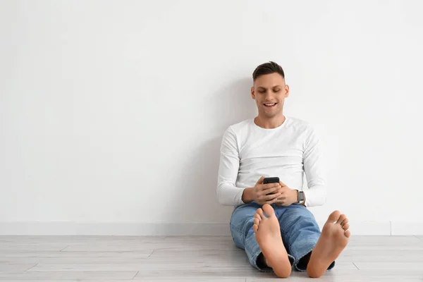 Young Barefoot Man Using Mobile Phone Light Wall — Stock Photo, Image