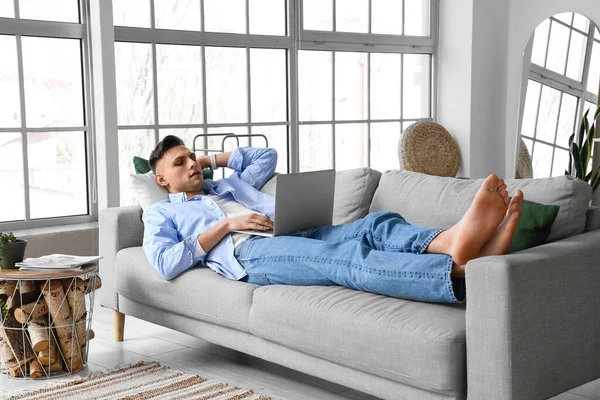 Young barefoot man using laptop on sofa at home