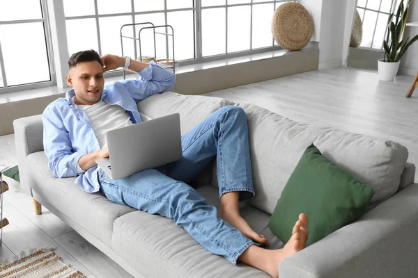 若いです裸足男使用ラップトップ上のソファにホーム — ストック写真
