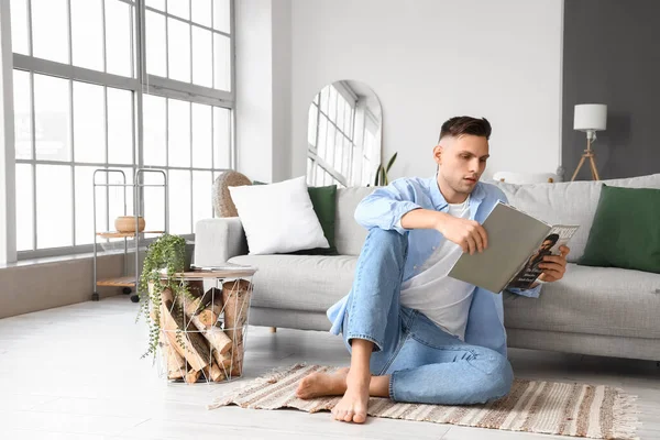 Young barefoot man reading magazine at home