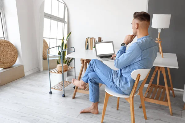 Young barefoot man using laptop at home