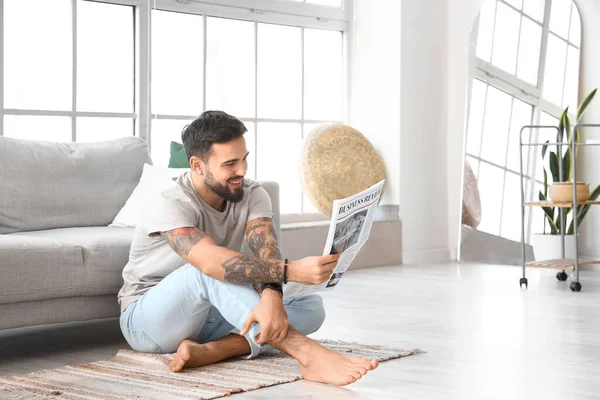 Handsome barefoot man reading newspaper at home