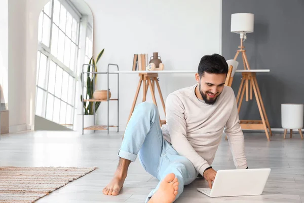 Handsome barefoot man using laptop on floor at home