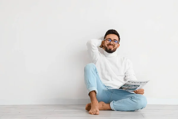 Handsome barefoot man reading newspaper near light wall