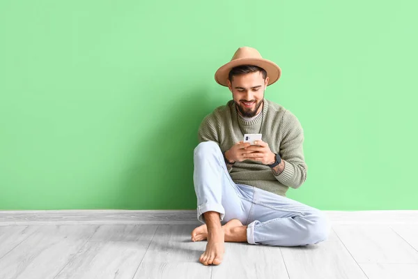 Handsome barefoot man using mobile phone near green wall