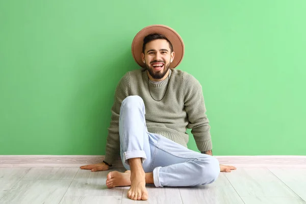 Handsome barefoot man in hat sitting near green wall