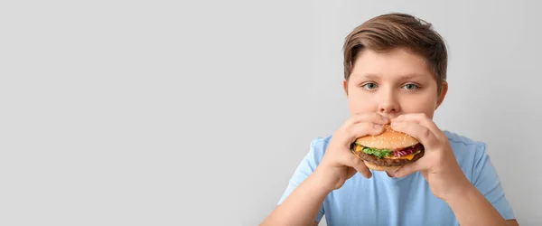 太りすぎの少年はテキストのためのスペースと軽めの背景にハンバーガーを食べる — ストック写真