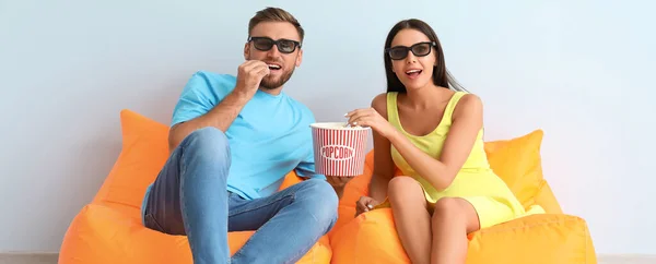 Young couple watching movie on light background