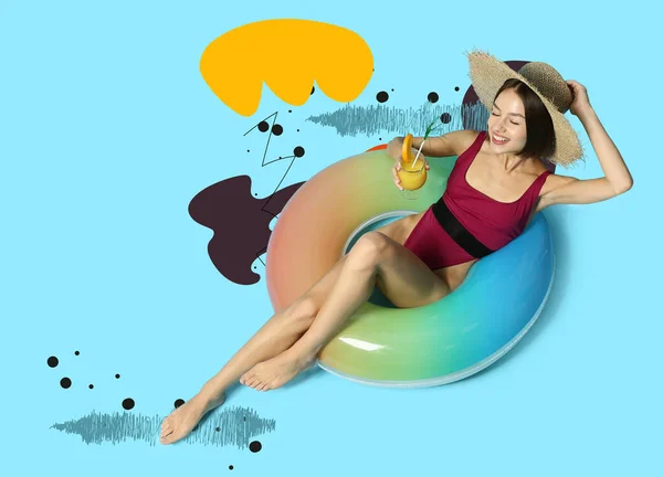Young woman with cocktail and inflatable ring on blue background