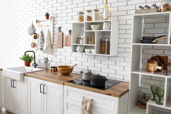 Shelf unit with jars and kitchen counters with utensils near white brick wall