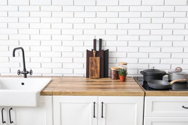 Mutfak tezgahları lavabo, kesme tahtaları ve çatal bıçakları beyaz tuğla duvarın yanında.