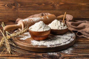 Tahta arka planda un, oklavalı iğne ve buğday kulaklı kaseler.