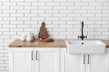 Modern lavabosu olan mutfak tezgahı ve beyaz tuğla duvarın yanında farklı aletler.