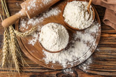 Tahta arka planda un, oklavalı iğne ve buğday kulaklı kaseler.