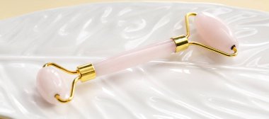 Beyaz arkaplanda gül kuvars yüz masajı silindiri, yakın plan