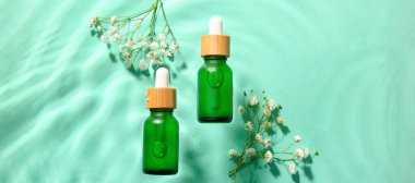 Kozmetik serumu şişeleri ve renk arka planında sudaki çiçekler.