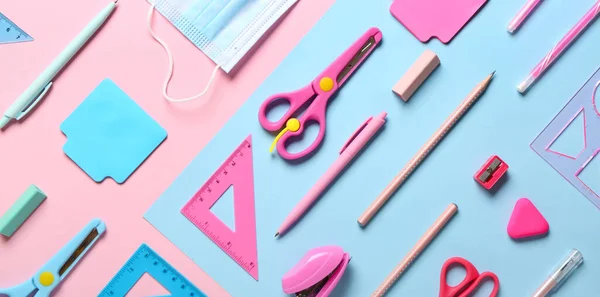 Different school supplies and medical mask on colorful background, top view