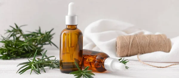 Bottles of healthy rosemary essential oil on light background