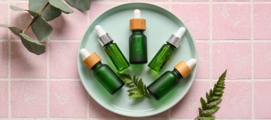 Pembe arka planda doğal kozmetik serumu şişeleriyle kaplanmış.