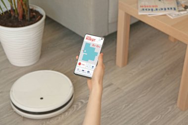 Cep telefonu ve modern uzaktan kumandalı robot elektrikli süpürgesi olan bir kadın.