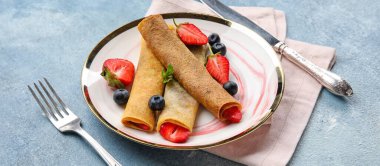 Mavi arka planda böğürtlen ve çatal bıçaklı ince krep tabağı.