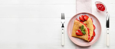 Üzerinde çilek, çatal bıçak ve reçel bulunan ince krep tabağı.