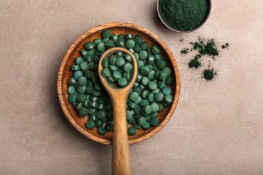 Kaseler dolusu spirulina tozu, haplar ve bej arka planda kaşık