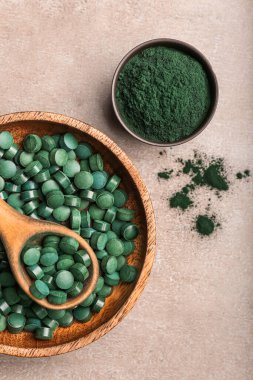 Kaseler dolusu spirulina tozu, haplar ve bej arka planda kaşık