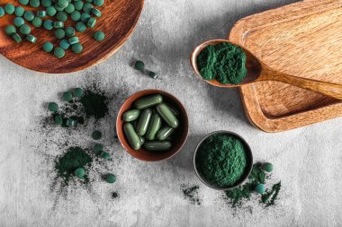 Kaseler dolusu spirulina tozu ve arkaplanda haplar.