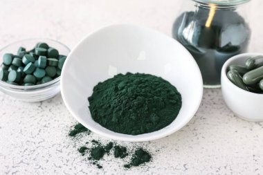 Kaseler dolusu spirulina tozu ve arkaplanda haplar.