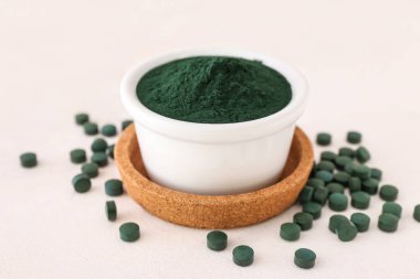 Bir kase yeşil spirulina tozu ve beyaz arka planda haplar.