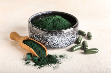 Beyaz arka planda bir kase spirulina tozu, kepçe ve haplar.