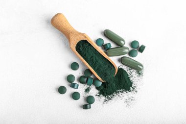 Bir top spirulina tozu ve beyaz arka planda haplar.